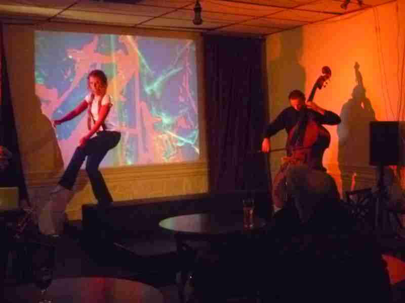 A dancer and a bass player performing in front of abstract projected images.