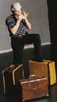 Poster image for Mangiacake showing Charly Chiarelli standing with suitcases playing a harmonica.