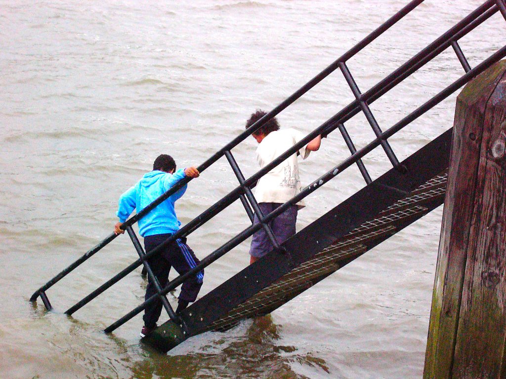 Two boys climbing down a ladder over the Thames