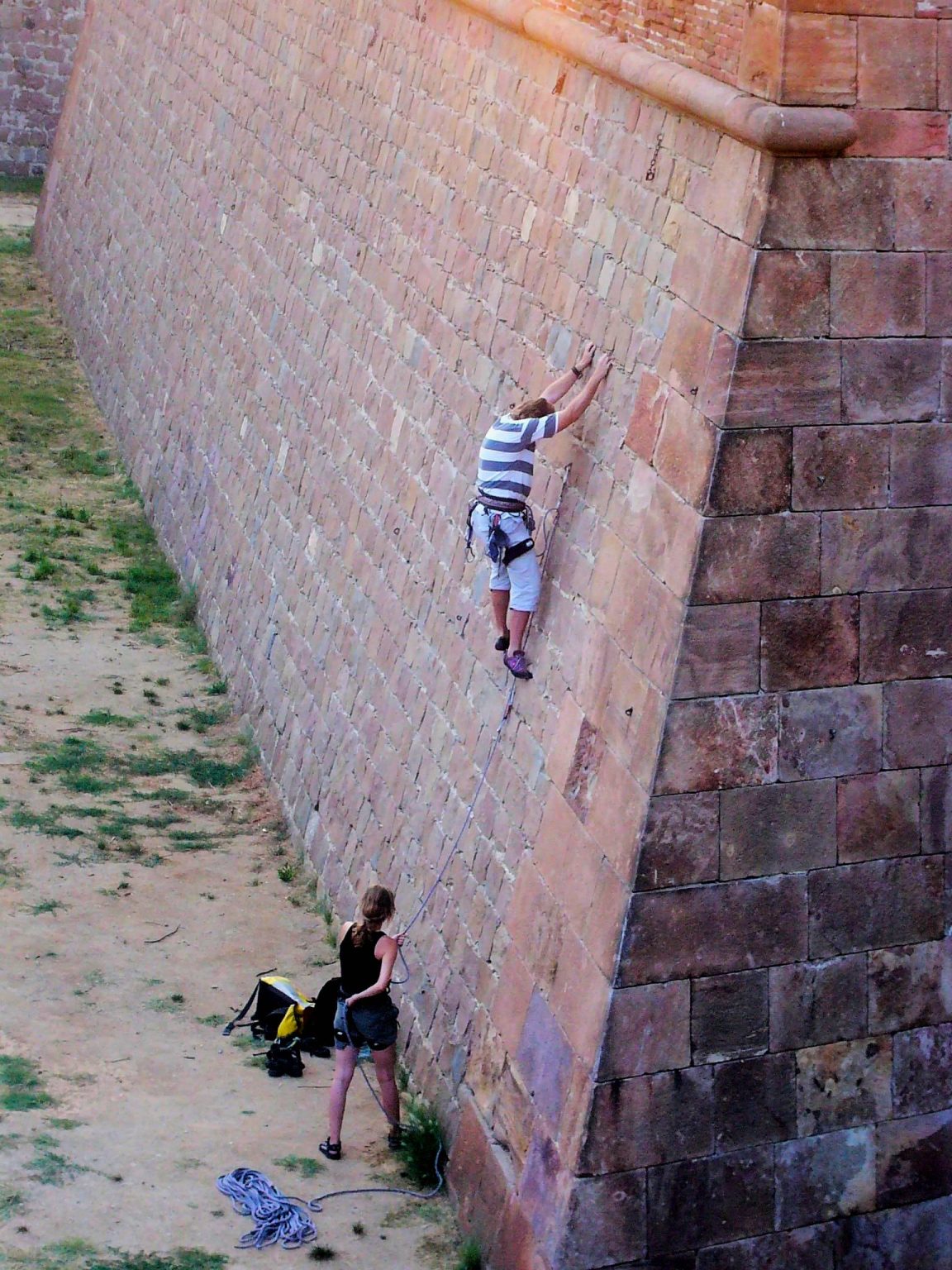 A man climbing a wall, a woman holding the safety rope from below.