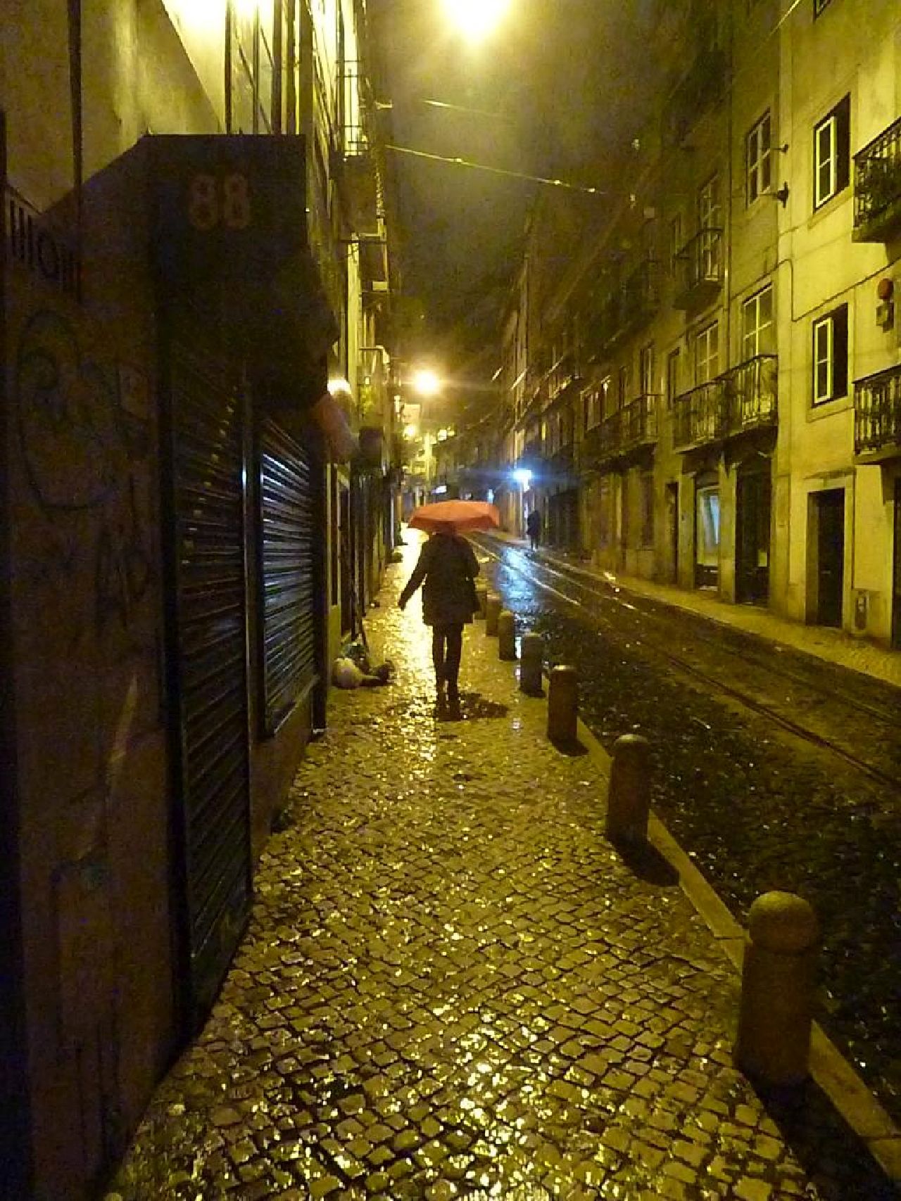 A figure with an unbrella walking away on a lonely night street in Lisbon.